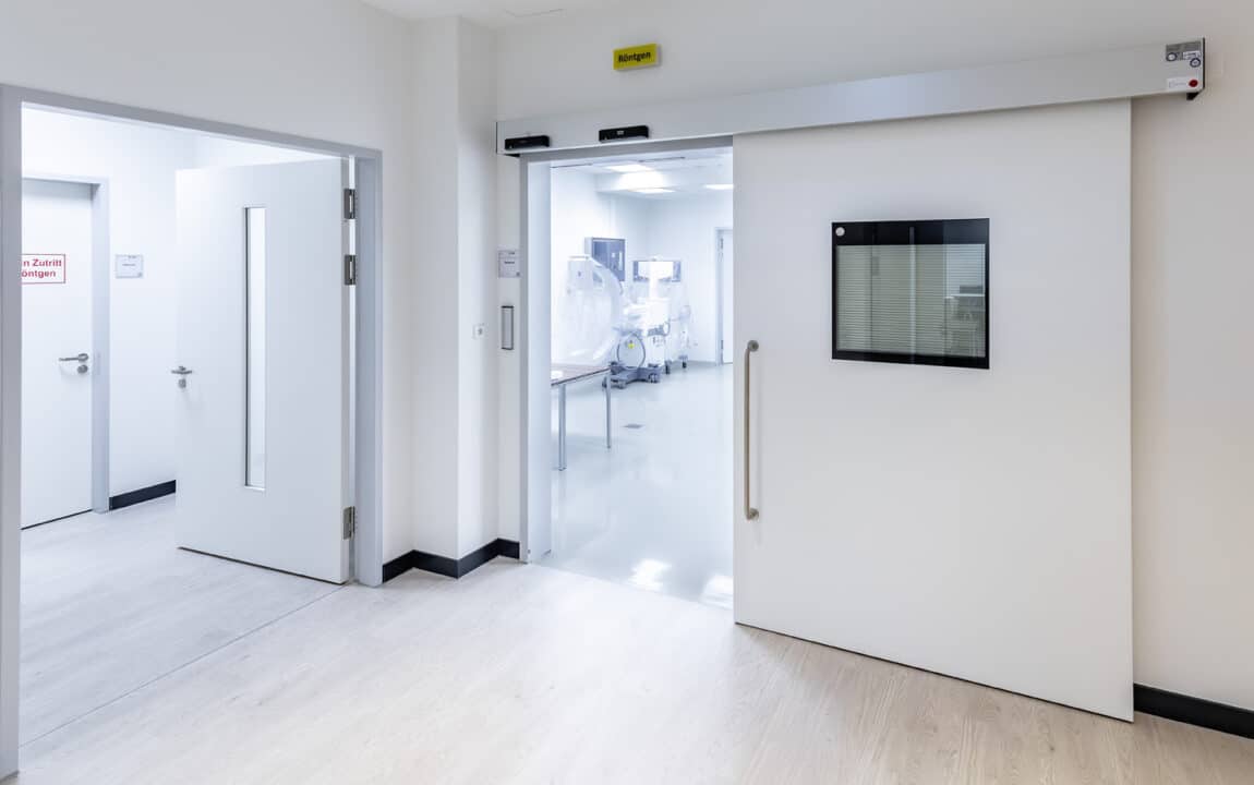 Geöffnete automatische Strahlenschutz-Schiebetür eines Röntgenraums mit Blick auf medizinische Bildgebungstechnik im klinischen Untersuchungsbereich.