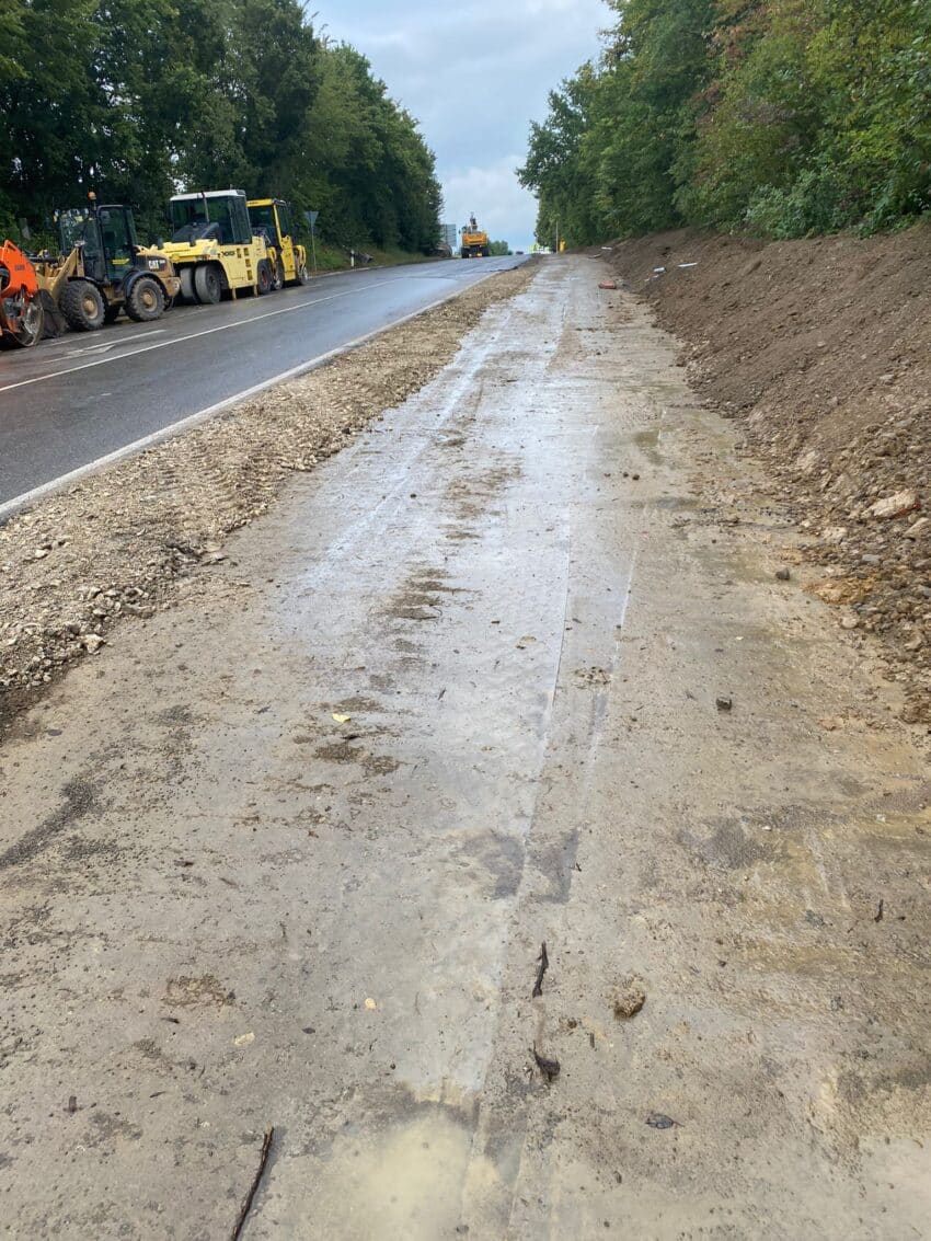 Baustelle eines Radwegs neben einer Landstraße mit Baumaschinen und vorbereiteter Fahrbahnkante.