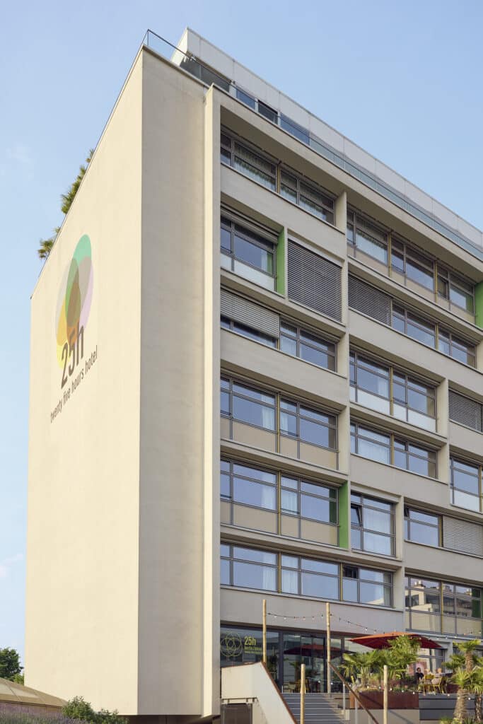 Moderne Fassade des 25hours Hotel Bikini Berlin mit Logo auf hellem Putz, großen Fensterflächen und Dachterrasse mit Pflanzen