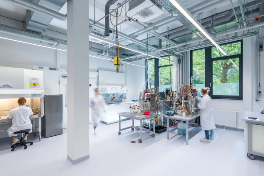 Drei Forscherinnen arbeiten in einem hellen, modernen Labor mit Hightech-Geräten und Labortischen.