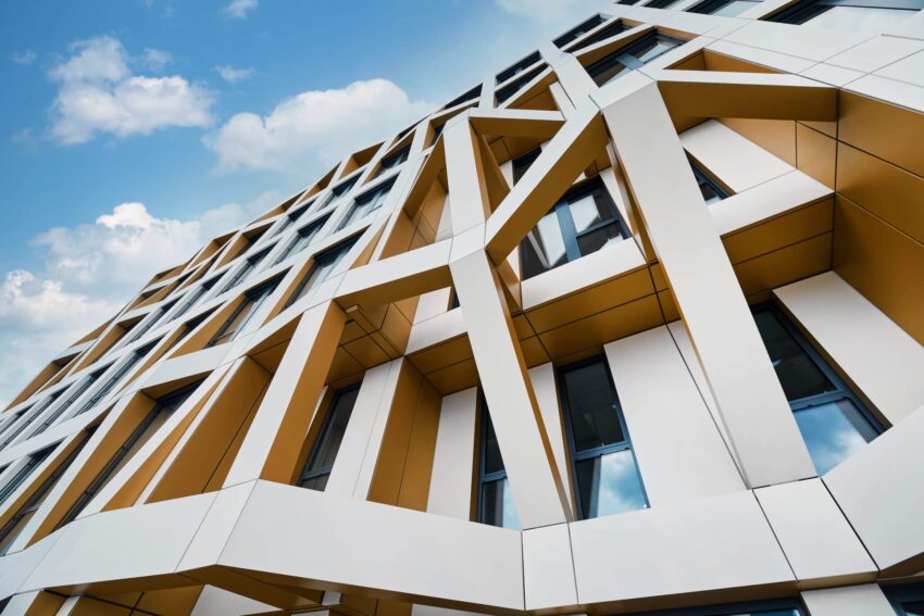 Schräg aufgenommene Außenansicht eines Bürogebäudes mit markanter, strukturierter Fassade in Weiß-Gold.