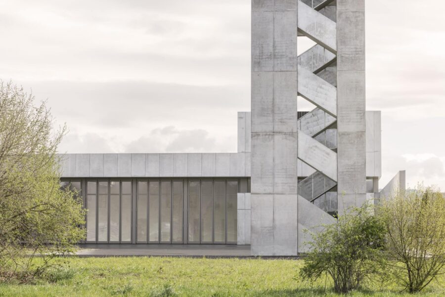 Moderne Betonarchitektur mit vertikalem Treppenturm und klarer Fassadengliederung, aufgenommen in natürlicher Umgebung bei weichem Tageslicht.