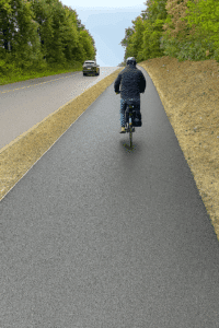 Radfahrer fährt auf einem frisch asphaltierten Radweg entlang einer Landstraße, Visualisierung der geplanten Strecke.