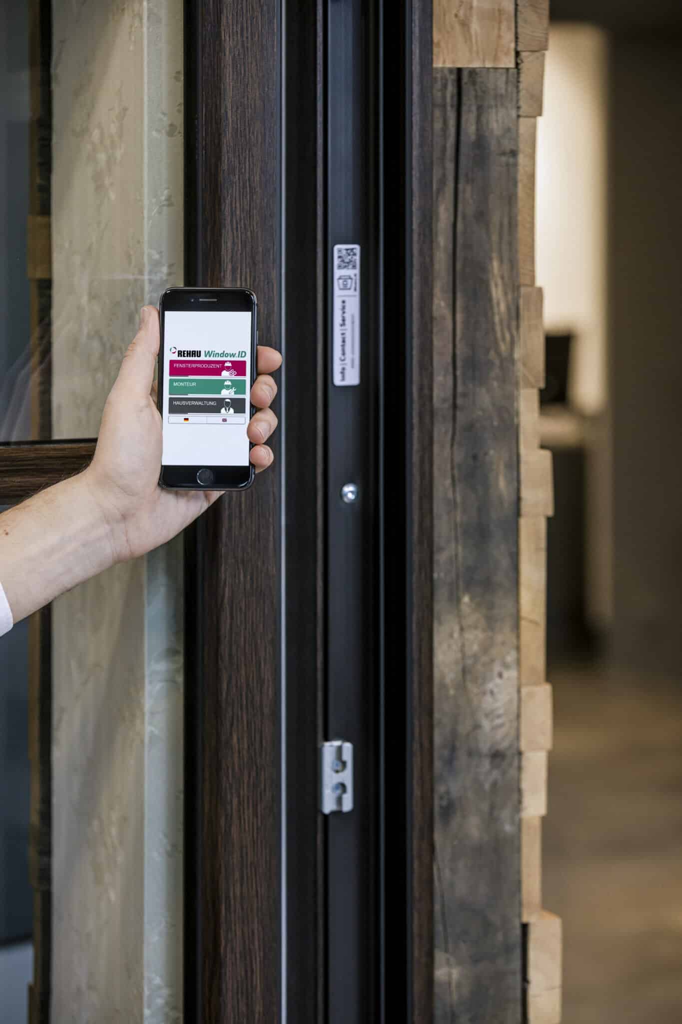 Hand hält Smartphone vor Fensterrahmen und scannt REHAU Window ID zur digitalen Identifikation und Serviceabfrage.