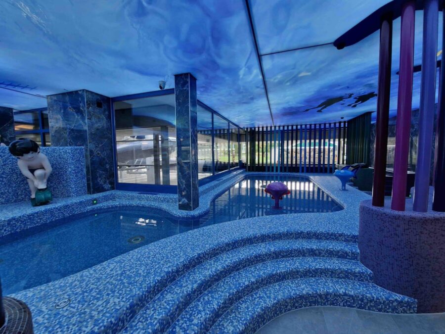 Innenpool mit aufwendig gestalteter Decke in Unterwasseroptik, Glasfront und farbigen Designelementen.