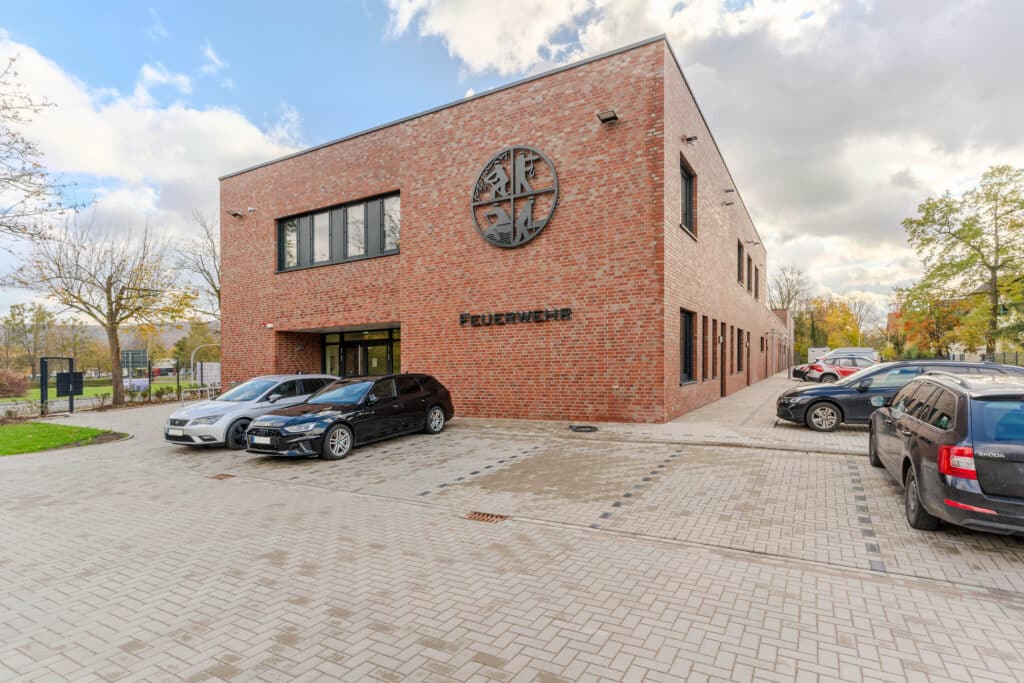 Ansicht des Haupteingangs der Feuerwache Bad Pyrmont mit Klinkerfassade, Feuerwehrlogo und Parkplatz.