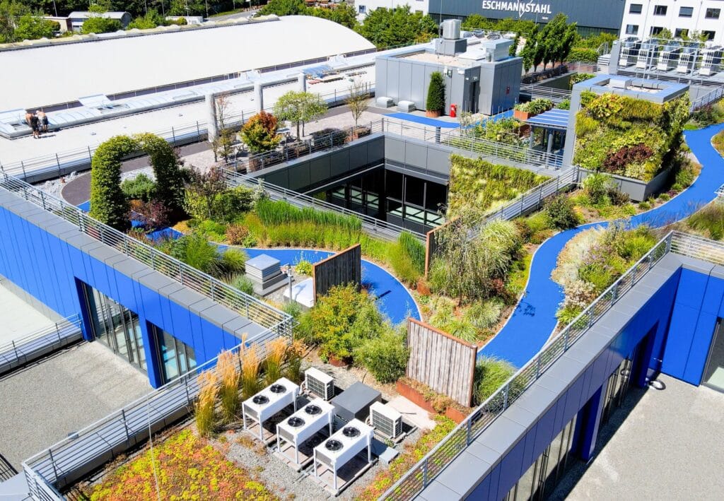 Begrünte Dachlandschaft eines Firmengebäudes mit geschwungenen Wegen, Pflanzbereichen, vertikalen Gärten und technischen Aufbauten in moderner Architektur.