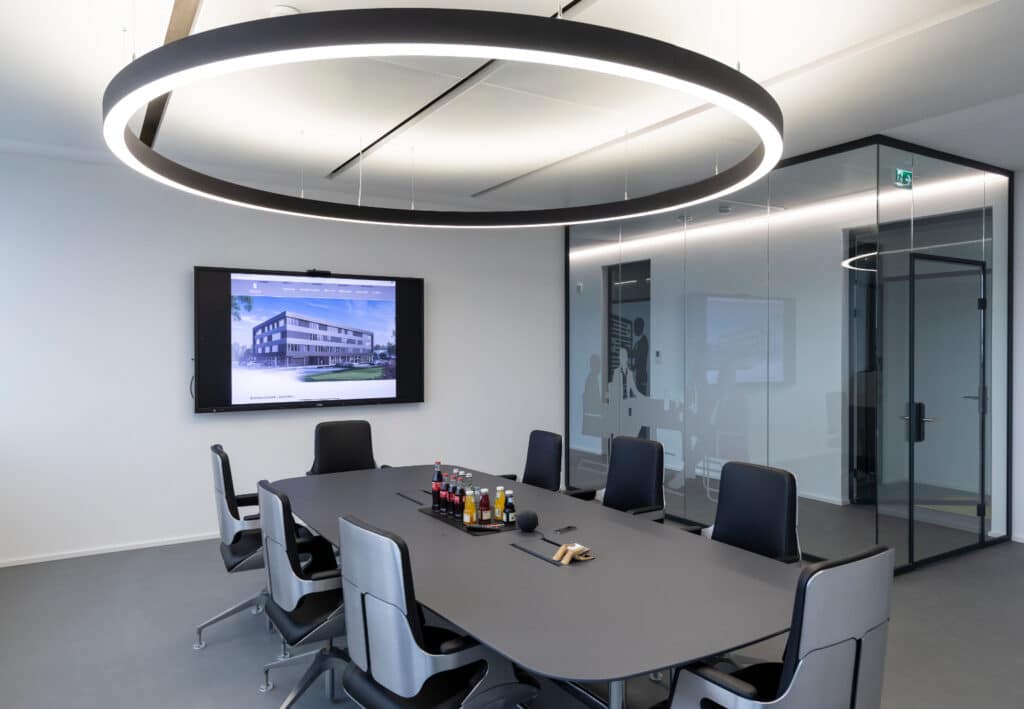 Moderner Besprechungsraum mit großem Konferenztisch, Bildschirm und Glaswänden im Businesspark.