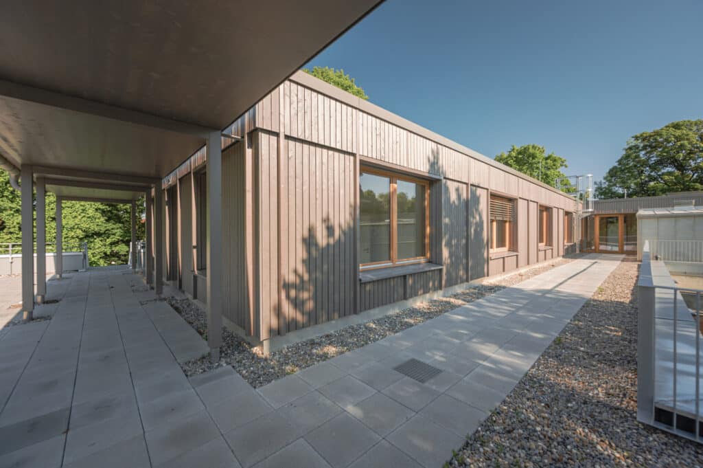 Büroerweiterung in der Scheinerstraße mit moderner Holzfassade, großen Fenstern und überdachtem Gehweg.