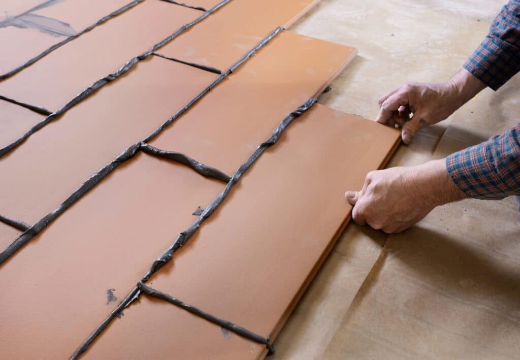 Handwerker verlegt Estrichziegel-Elemente mit Kleberfugen auf vorbereiteter Fläche – detailgenaue Montage im Trockenbauverfahren.