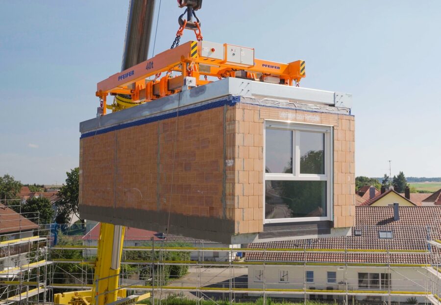 Ziegelmodul wird auf der Baustelle mit einem Kran und einem 40-Tonnen-Hebegestell präzise auf seine Position gehoben.