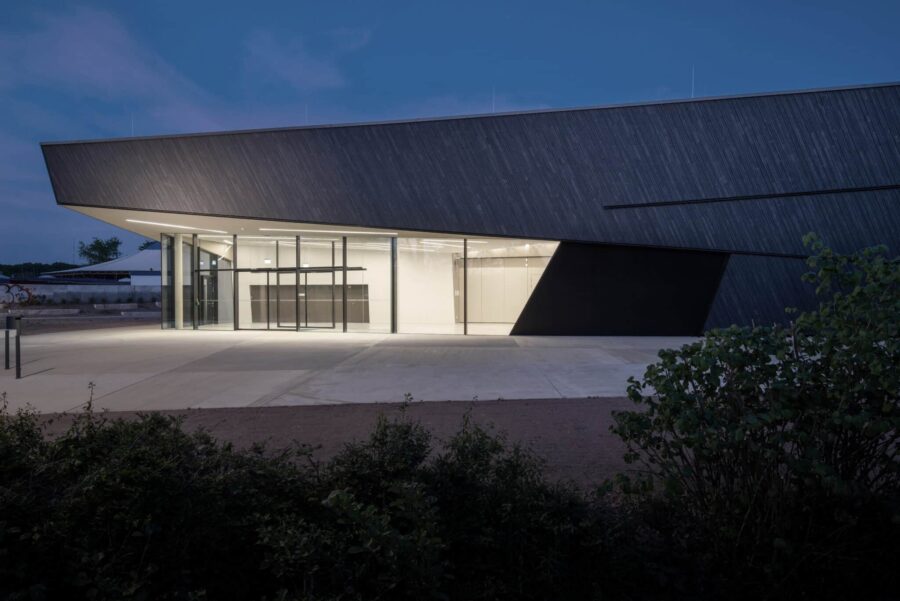 Moderne Veranstaltungshalle in Kuppenheim bei Nacht, beleuchteter Eingangsbereich mit großflächiger Glasfassade und dynamischer Dachform.