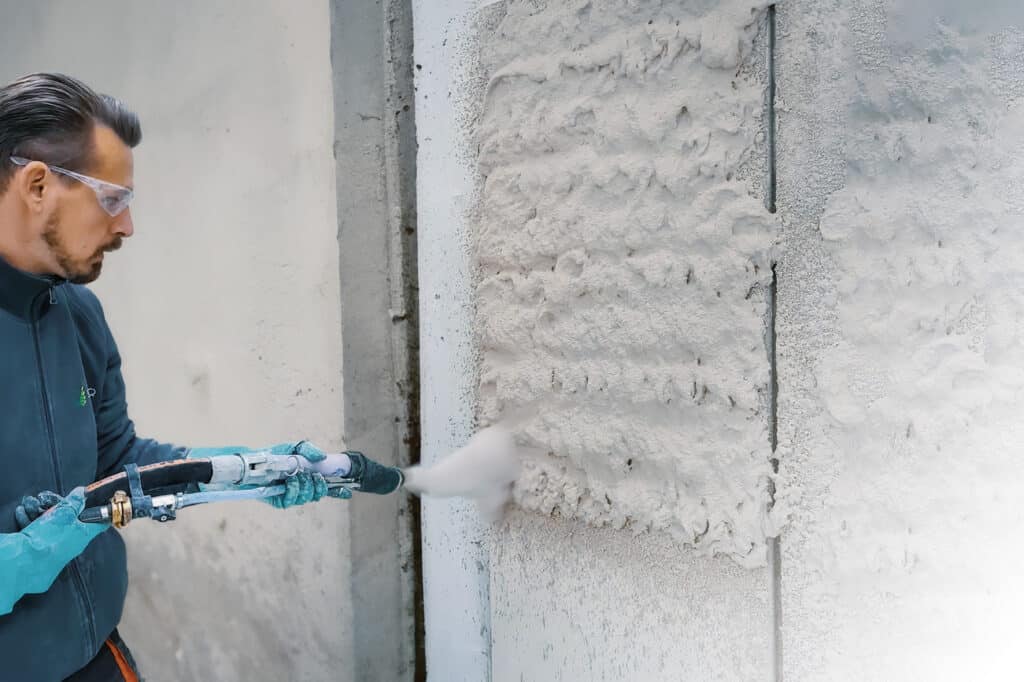 Handwerker beim maschinellen Auftragen von Dämmputz auf eine Fassade.