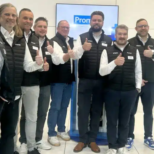 Gruppenfoto des Promat-Teams mit acht Mitarbeitenden, die in schwarzen Westen und weißen Hemden stehen und Daumen nach oben zeigen.