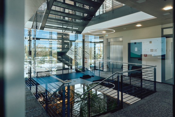 Innenansicht eines modernen Bürogebäudes mit offener Treppe, Glasfront und viel Tageslicht.