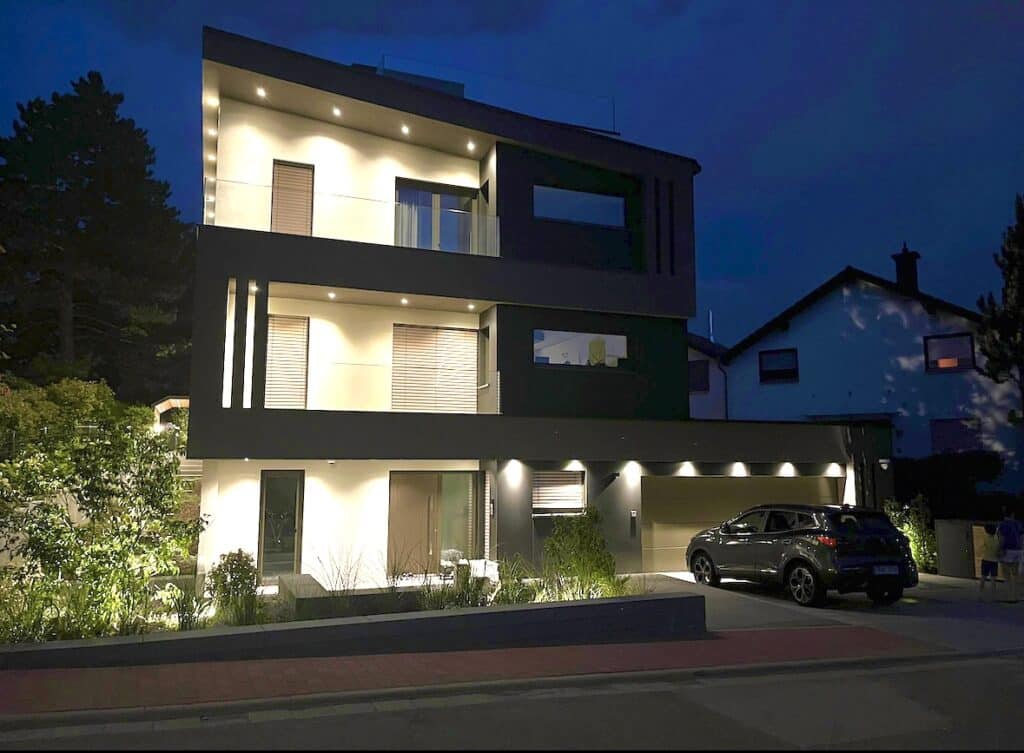 Stimmungsvolle Nachtaufnahme eines modernen Wohnhauses mit beleuchtetem Vorgarten und Carport.
