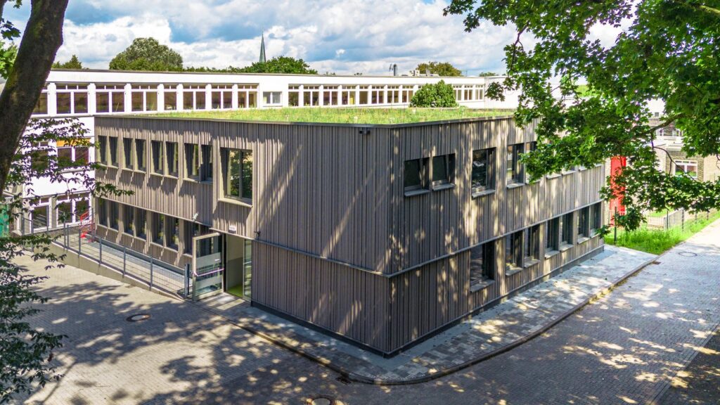 Modernes Schulgebäude in Holzmodulbauweise mit extensiv begrüntem Dach und großen Fensterflächen.