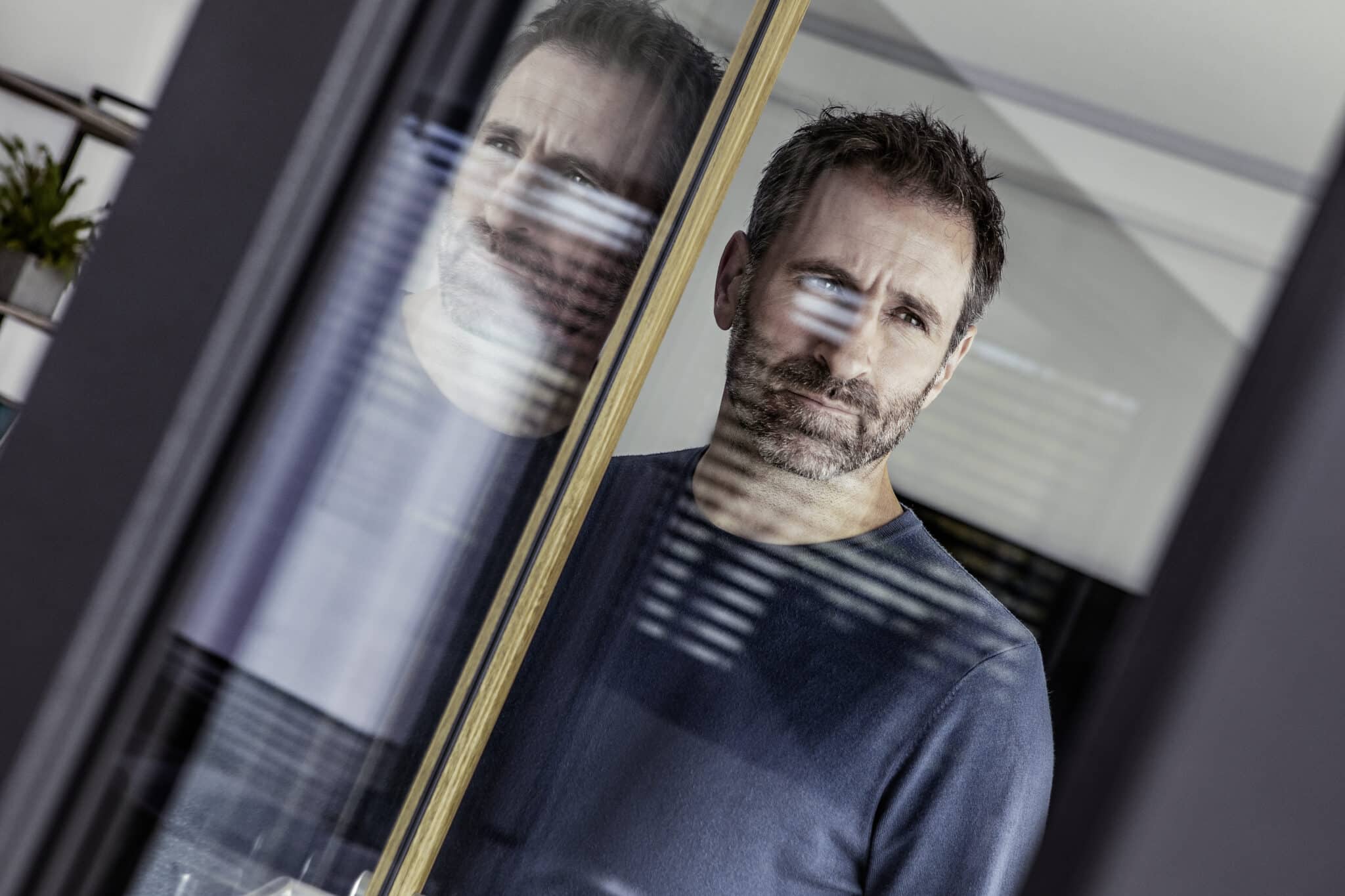 Ein Mann in einem dunklen Pullover steht vor dem Fenster