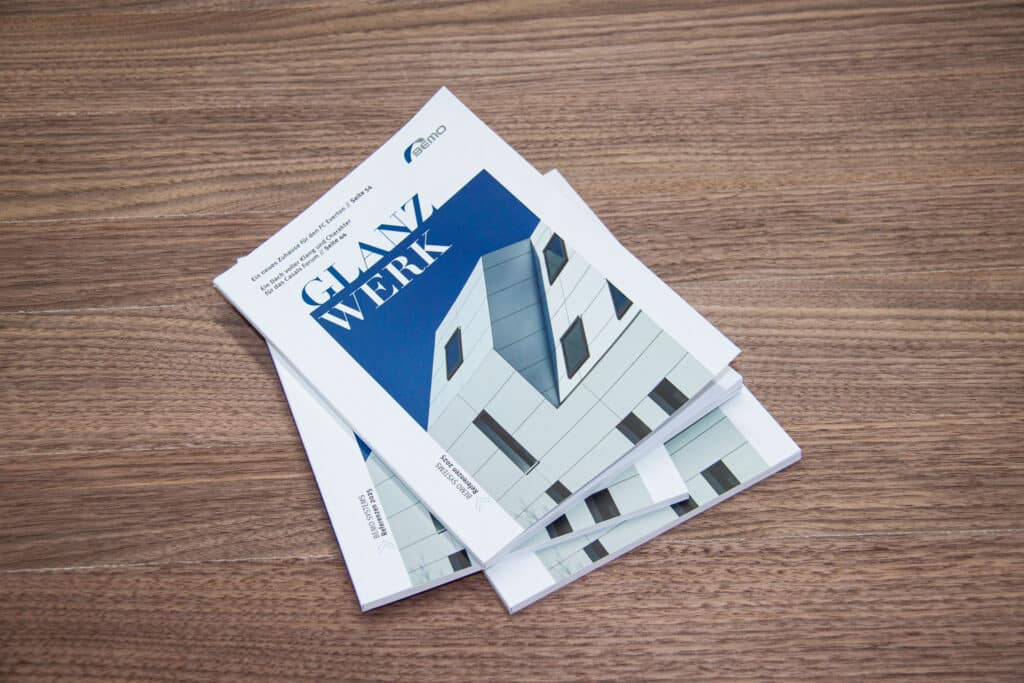 Mehrere Exemplare des GLANZWERK-Magazins von BEMO gestapelt auf einem Holztisch.