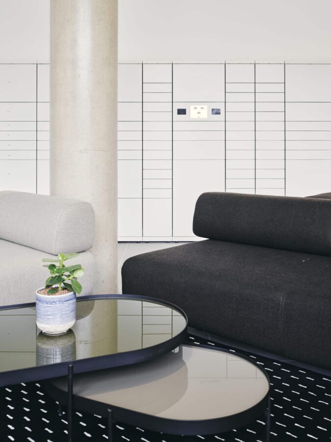 Detailaufnahme eines Sitzbereichs mit Sofas und runden Couchtischen vor einer weißen myRENZbox-Paketanlage.