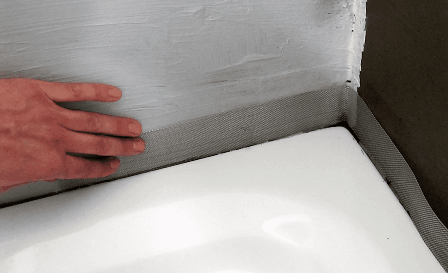 Hand drückt ein Schnittschutzband in die frisch aufgetragene Abdichtung an der Wand-Boden-Anschlussfuge einer Dusche oder Badewanne.