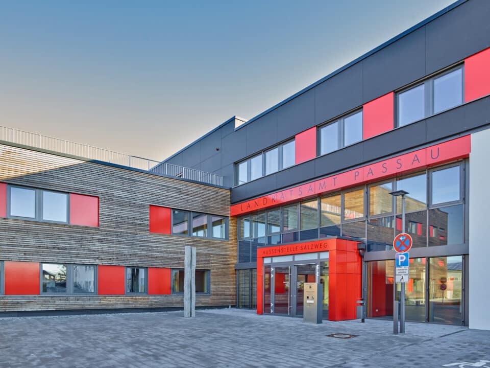 Moderner Neubau des Landratsamts Passau in Salzweg mit Holzfassade, roten Fassadenelementen und großzügigem Eingangsbereich im Passivhausstandard.