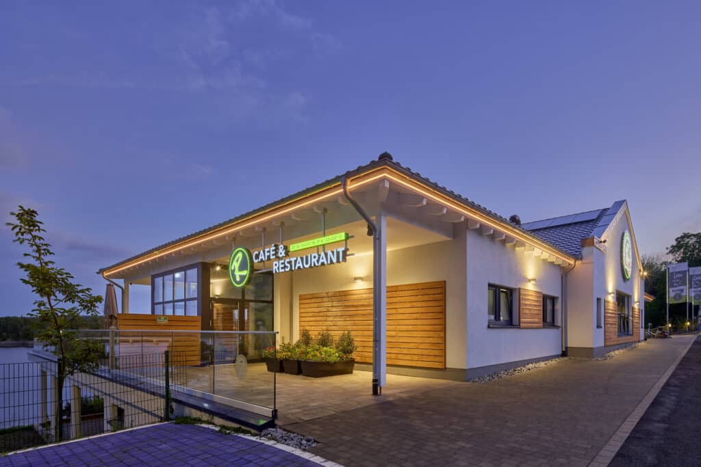 Beleuchtete Außenansicht des Cafés und Restaurants am Möhnesee in der Abenddämmerung.