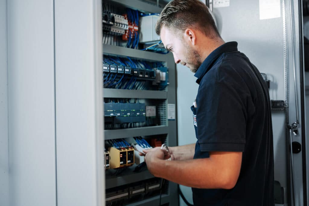 Ein Servicetechniker inspiziert die Elektronik und Verkabelung in einem Schaltschrank einer Aufzugsanlage.
