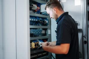 Ein Servicetechniker inspiziert die Elektronik und Verkabelung in einem Schaltschrank einer Aufzugsanlage.