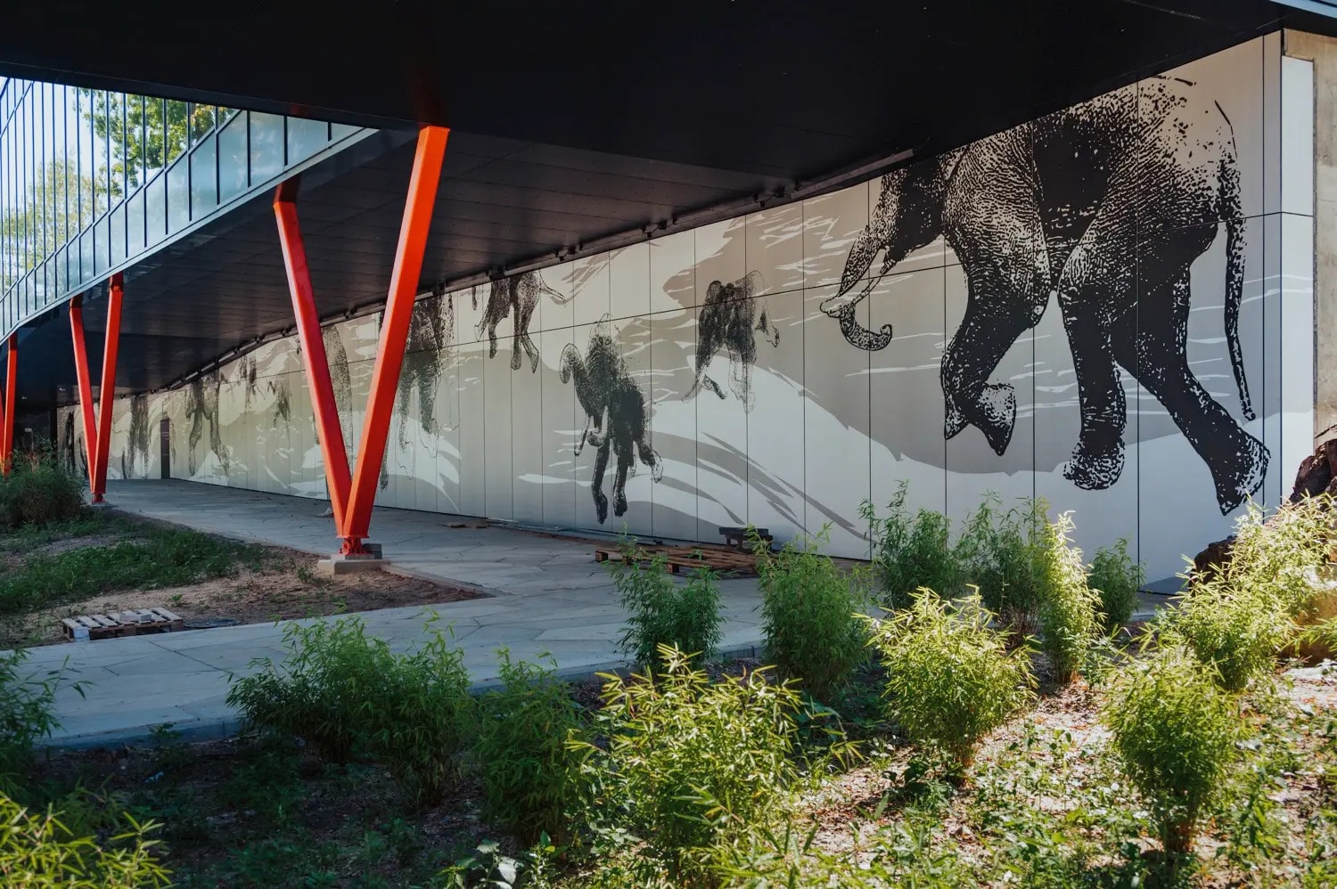 Fassadenverkleidung aus EQUITONE-Platten mit grafischem Elefantenmotiv am Orientarium, unterstützt durch markante orange Stahlstützen.
