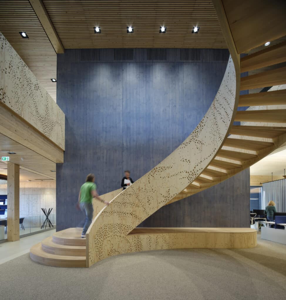 Moderne, geschwungene Holztreppe im Aquon-Gebäude, gestaltet von EeStairs, mit perforierter Oberfläche und offener Raumstruktur.
