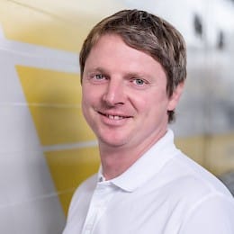 Portraitaufnahme von Markus Stuhlinger, Ingenieur bei best wood Schneider, mit weißem Poloshirt vor gelb-weißer Wand.