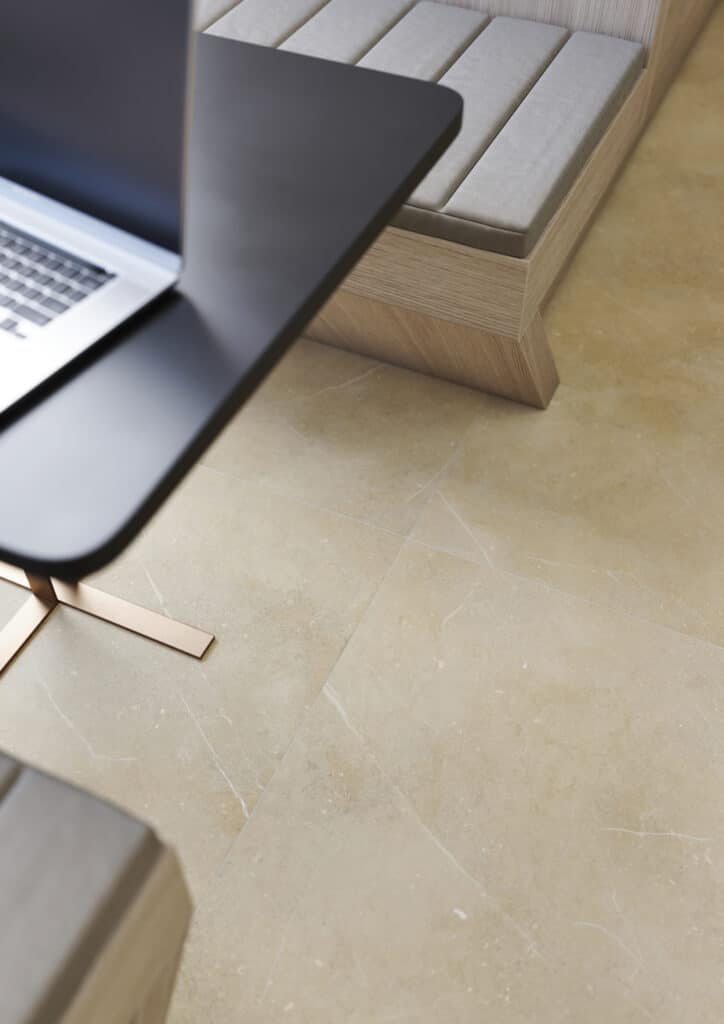 Detailansicht einer sandfarbenen Bodenfliese in Natursteinoptik unter einem schwarzen Tisch in einer modernen Lounge.