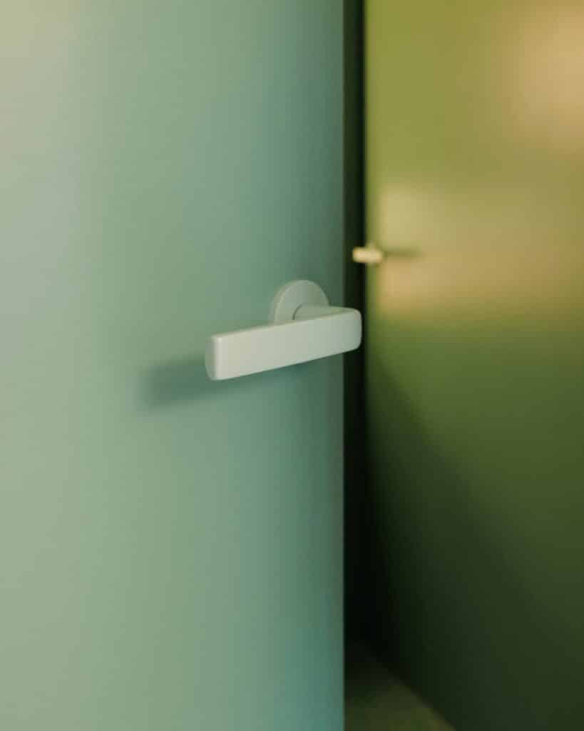 Nahaufnahme eines mintgrünen Türdrückers auf einer farblich passenden Tür in einem modernen Innenraum.