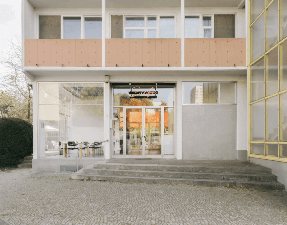 Eingang eines modernen Cafés in Berlin mit Glasfassade, Balkon und Neon-Schriftzug „Café“