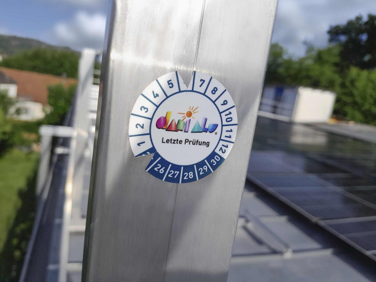 Nahaufnahme einer Prüfplakette auf einem Geländer zur Dokumentation der letzten Wartung einer Absturzsicherung