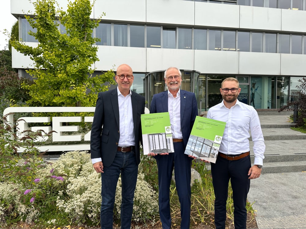 Drei Männer vor dem GEZE-Firmensitz halten zwei EPD-Urkunden für nachhaltige Türsysteme in den Händen.