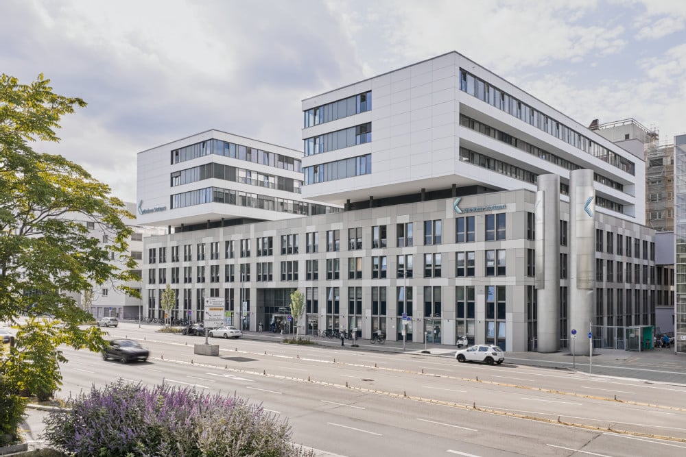 Außenansicht des Klinikums Stuttgart mit moderner, heller Fassadenstruktur, großflächigen Fensterbändern und verkehrsreicher Straße im Vordergrund.