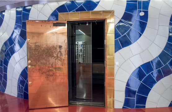 Geöffnete Eingangstür aus Kupfer mit kunstvoll gestalteter blauer Wandverkleidung in der Königlichen Bibliothek Stockholm.