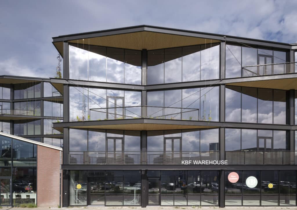 Vorderansicht des KBF Warehouse mit großflächigen Glasfassaden, begrünten Balkonen und markanter Stahlkonstruktion.