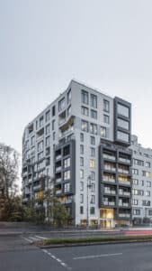 Fassade des Wohngebäudes HH74 in Berlin mit markanten Balkonen und großen Fensterflächen, aufgenommen bei einsetzender Dämmerung.