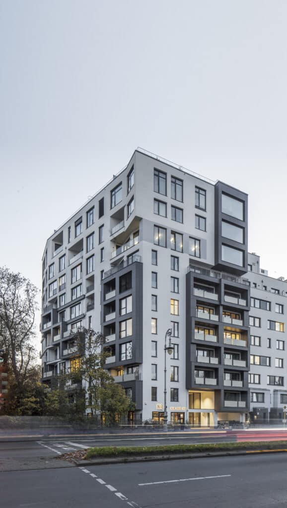 Fassade des Wohngebäudes HH74 in Berlin mit markanten Balkonen und großen Fensterflächen, aufgenommen bei einsetzender Dämmerung.