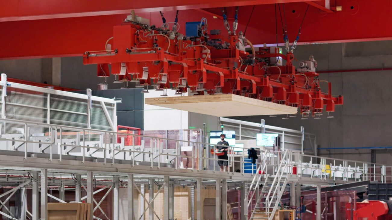 roßes CLT XL-Deckenelement wird mit rotem Hallenkran in einer Produktionshalle bewegt.