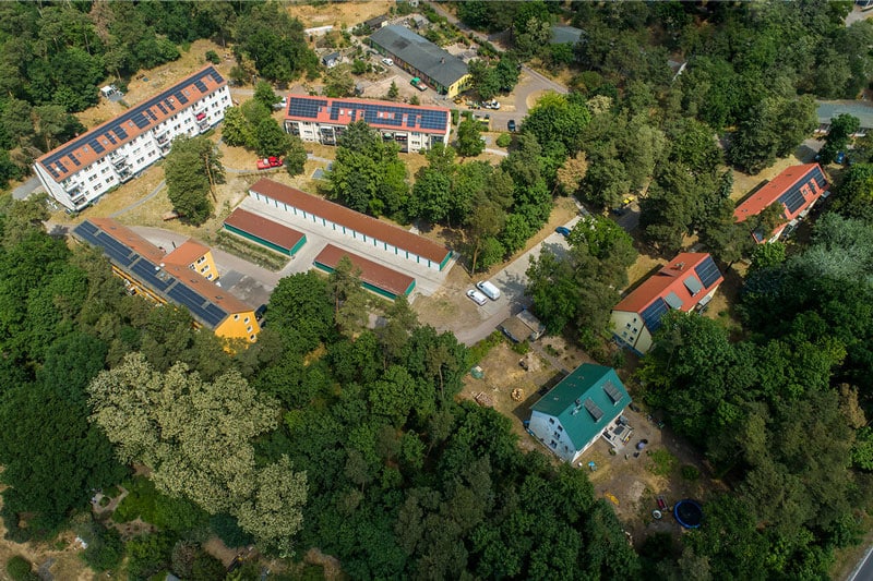 Luftbild eines Wohnquartiers mit mehreren Wohngebäuden, begrünter Umgebung und Solaranlagen auf den Dächern.