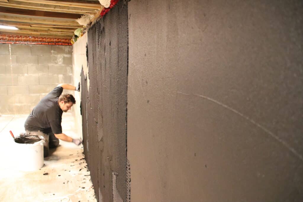 Handwerker trägt schwarze Leitschicht auf Betonwand auf – Arbeitsschritt zur Vorbereitung der Dichtungsprüfung.