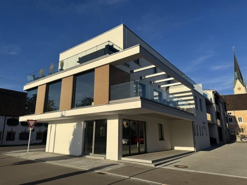 Moderne Eckfassade mit auskragendem Balkon, Glasgeländern und großflächigen Fenstern im urbanen Umfeld.