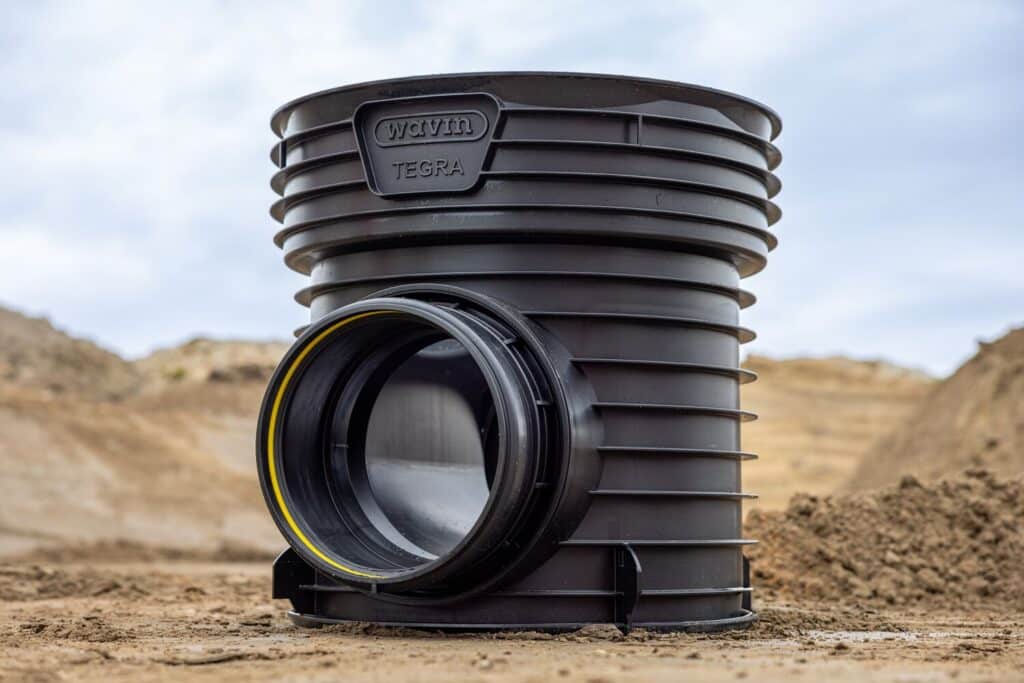 Schwarzes Wavin-Tegra-600-Schachtunterteil im Gelände, frontal mit seitlichem Rohranschluss.