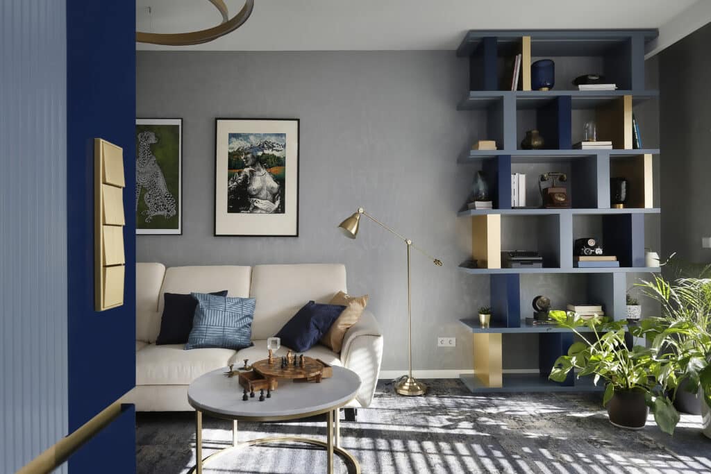 Stilvolles Wohnzimmer mit blauer Wand, goldfarbenem JUNG Schalter und dekorativem Wandregal.