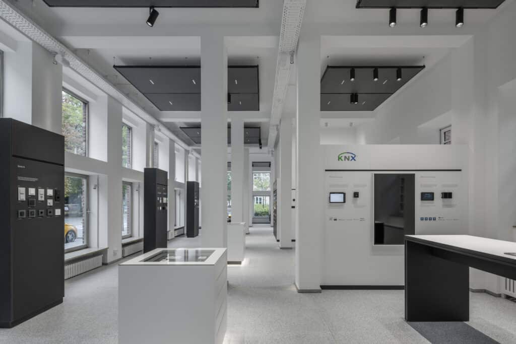 Großer Ausstellungsraum des JUNG Showrooms mit Produktdisplays, hoher Fensterfront und modernem Lichtkonzept.