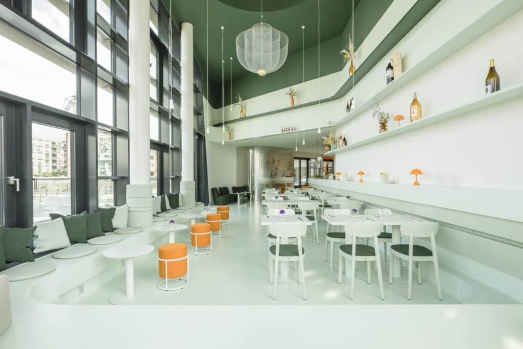 Innenansicht eines modernen Restaurants mit grüner und weißer Wandgestaltung sowie orangefarbenen Hockern